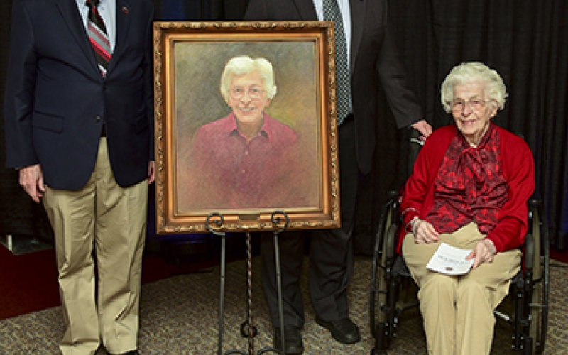 Photo of 2 men and a woman around a painted portrait of the woman