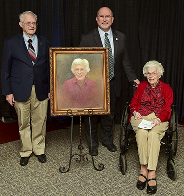 Photo of 2 men and a woman around a painted portrait of the woman