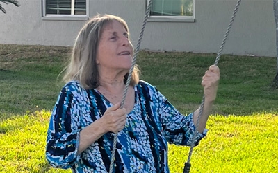 Adrienne Cohen swings on an outdoor swing hovering above a green lawn