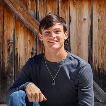 Photo of smiling male in sweatshirt and jeans in front of wooden fence